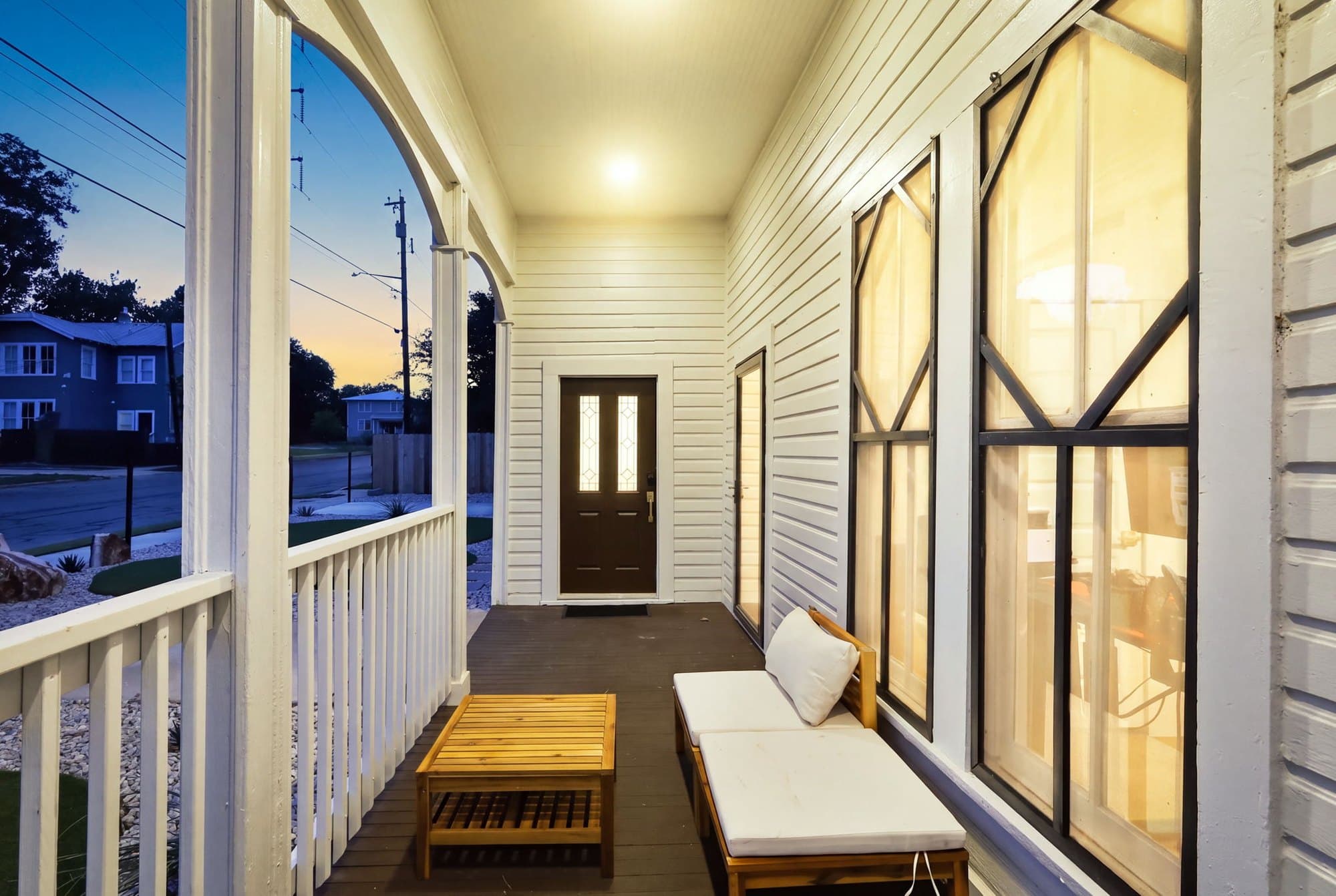 Side porch looking out to the street at dusk, warm light through the windows