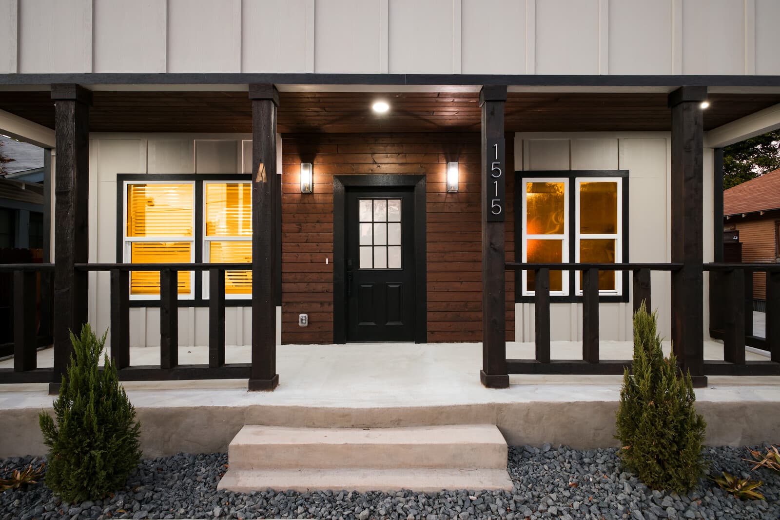 Covered front porch with dark stained columns and a black entry door, Kings Modern Residence, San Antonio