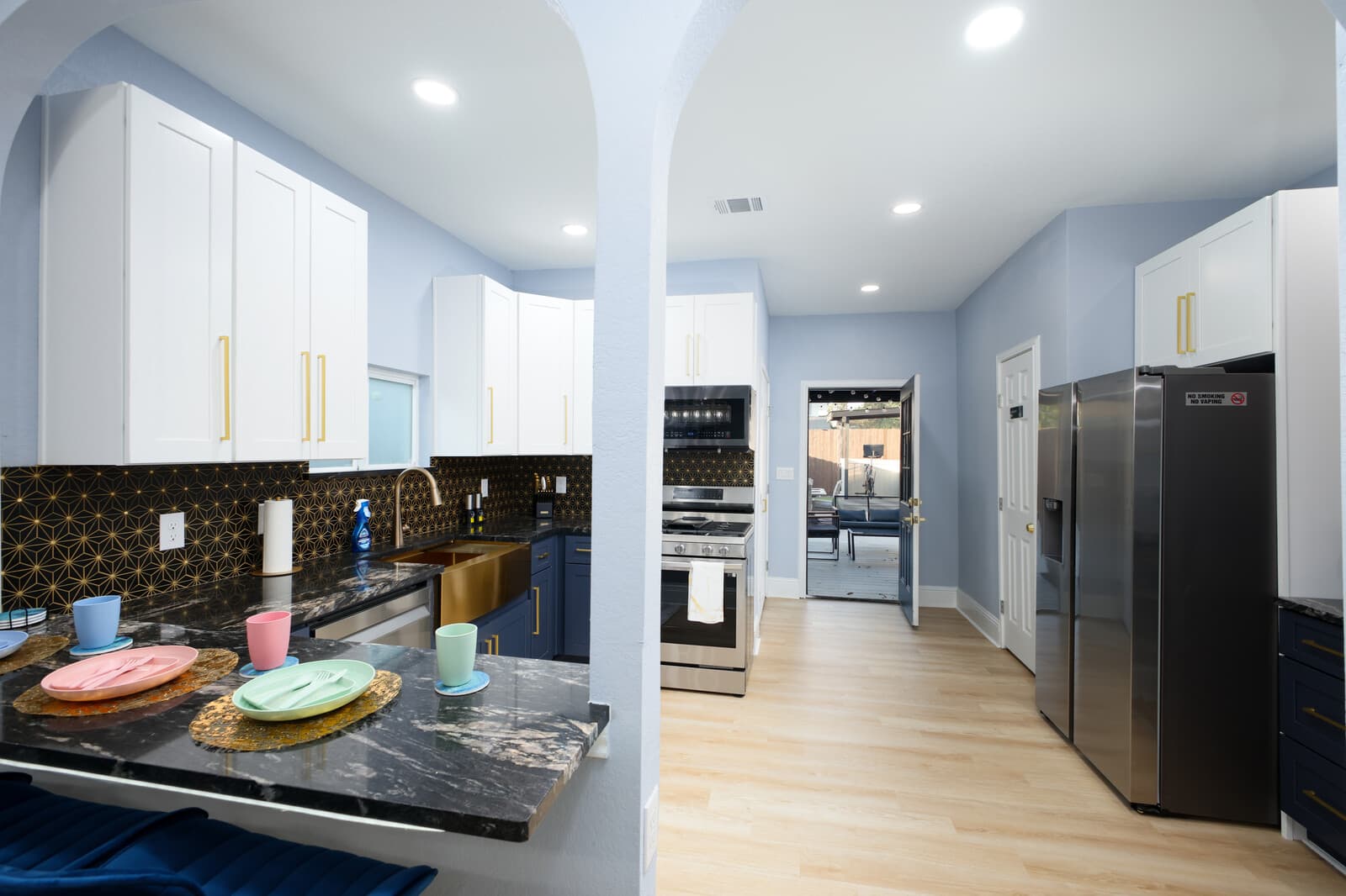 Main kitchen with white cabinetry, brass hardware and a patterned dark tile backsplash